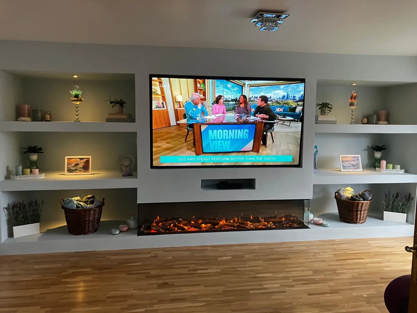 Built-in media wall with lit alcove shelving and an inset electric fire