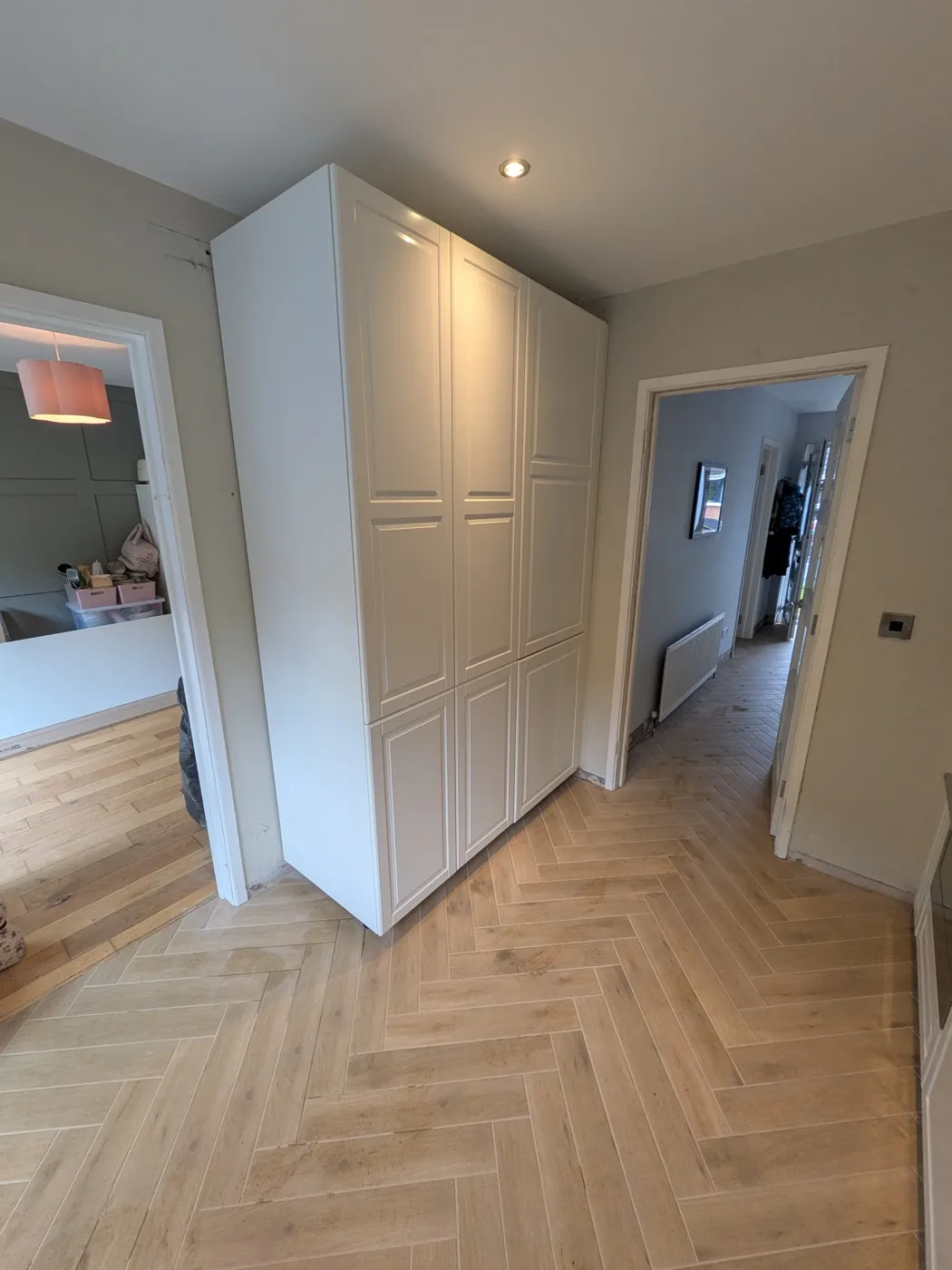 Cream panelled tall larder units on a herringbone wood-effect floor