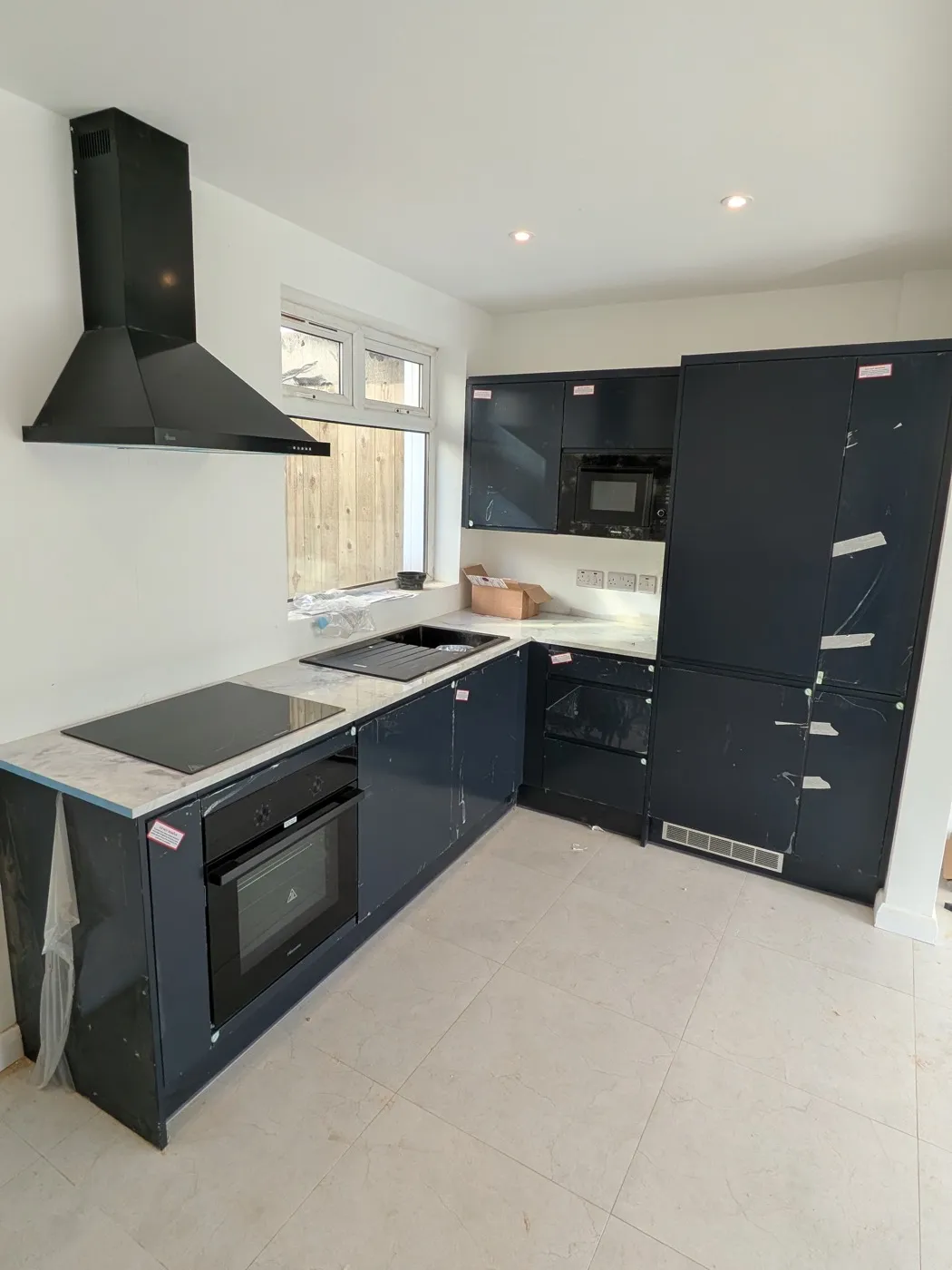 Navy gloss L-shaped kitchen with a black chimney hood and light stone worktops