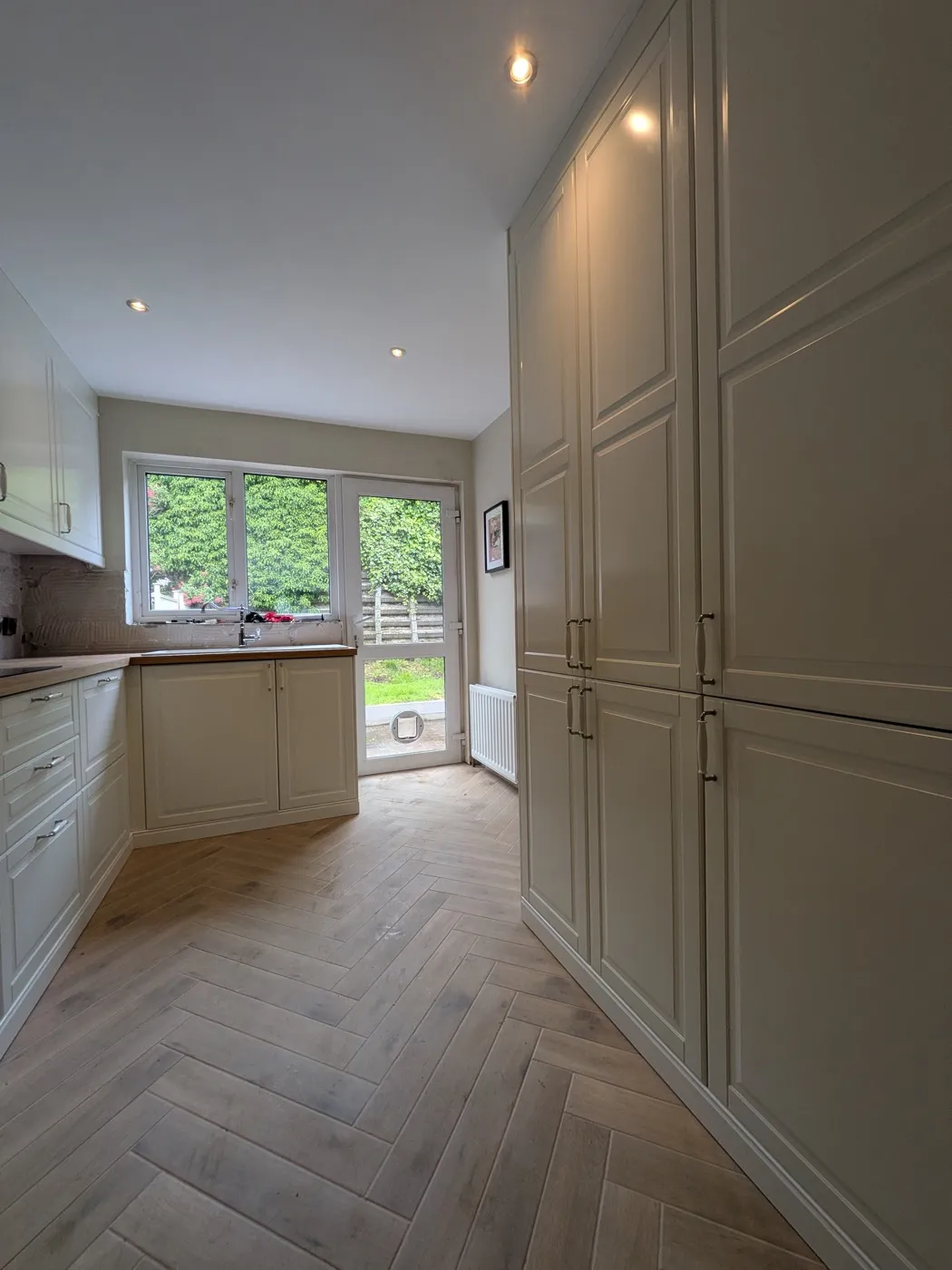 Cream panelled galley kitchen with tall larder units and garden doors