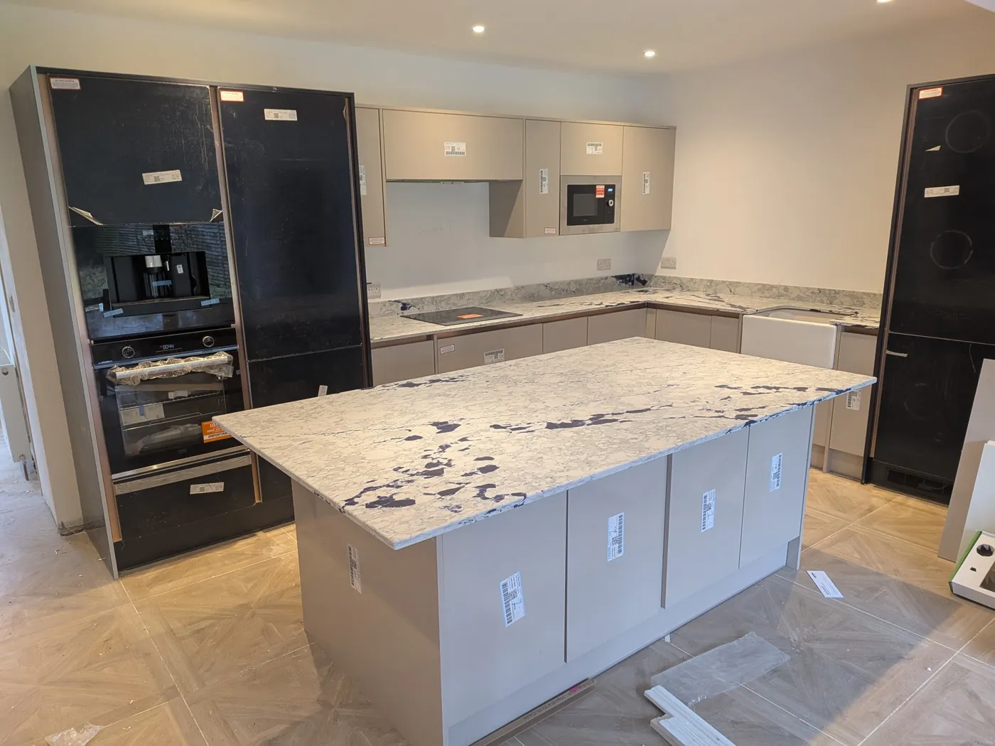 Kitchen with a large marble-effect island and black appliance housings, during installation