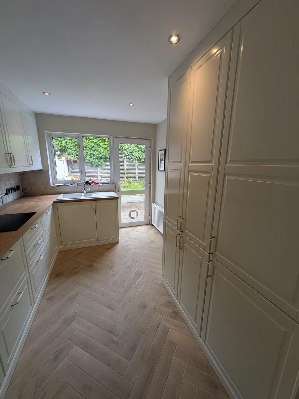 Cream galley kitchen with tall panelled units leading to garden doors