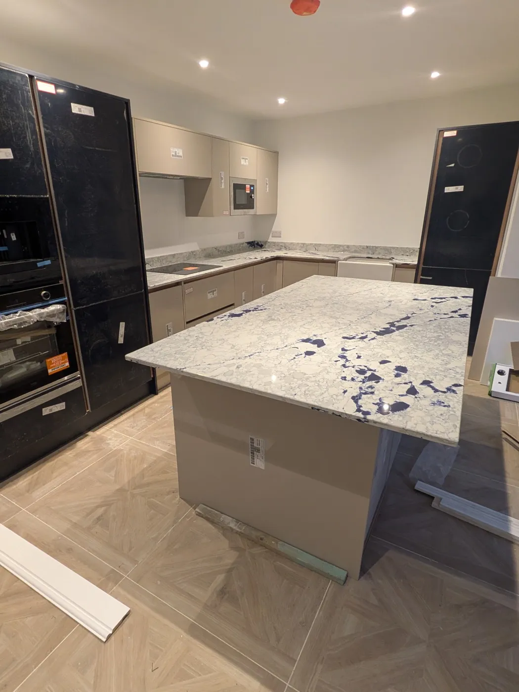 Cashmere kitchen island with a marble-effect worktop, between black tall units