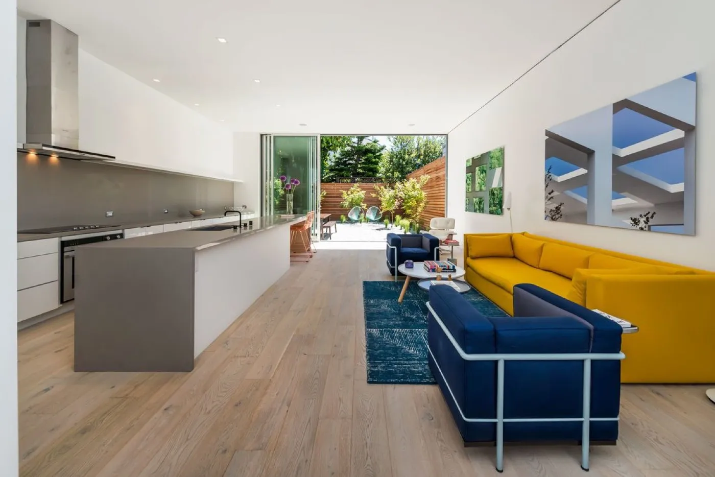 Open-plan kitchen and lounge with a white island and a view to a timber-fenced garden