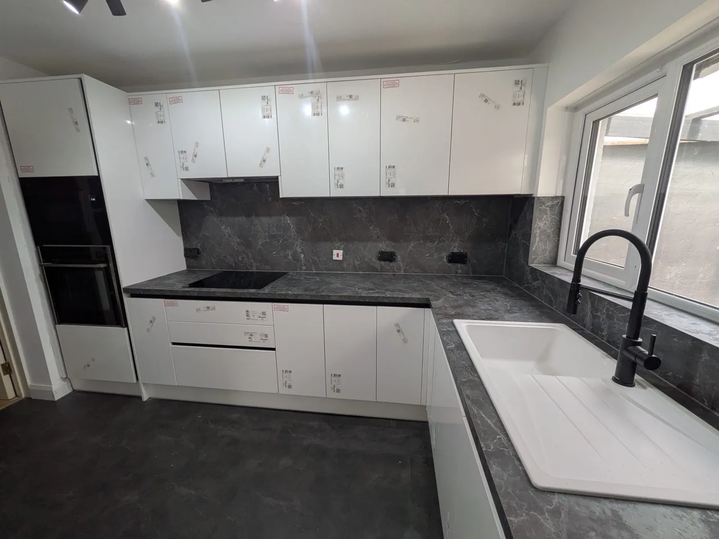 Newly fitted white gloss handleless kitchen with dark stone-effect worktops and a white ceramic sink