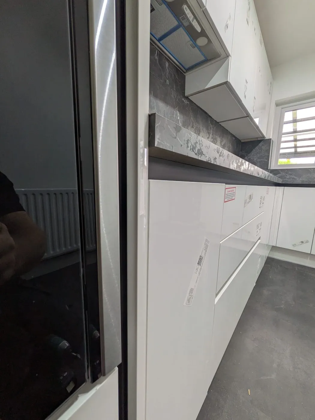White gloss kitchen units with a dark stone-effect splashback, protective film still on