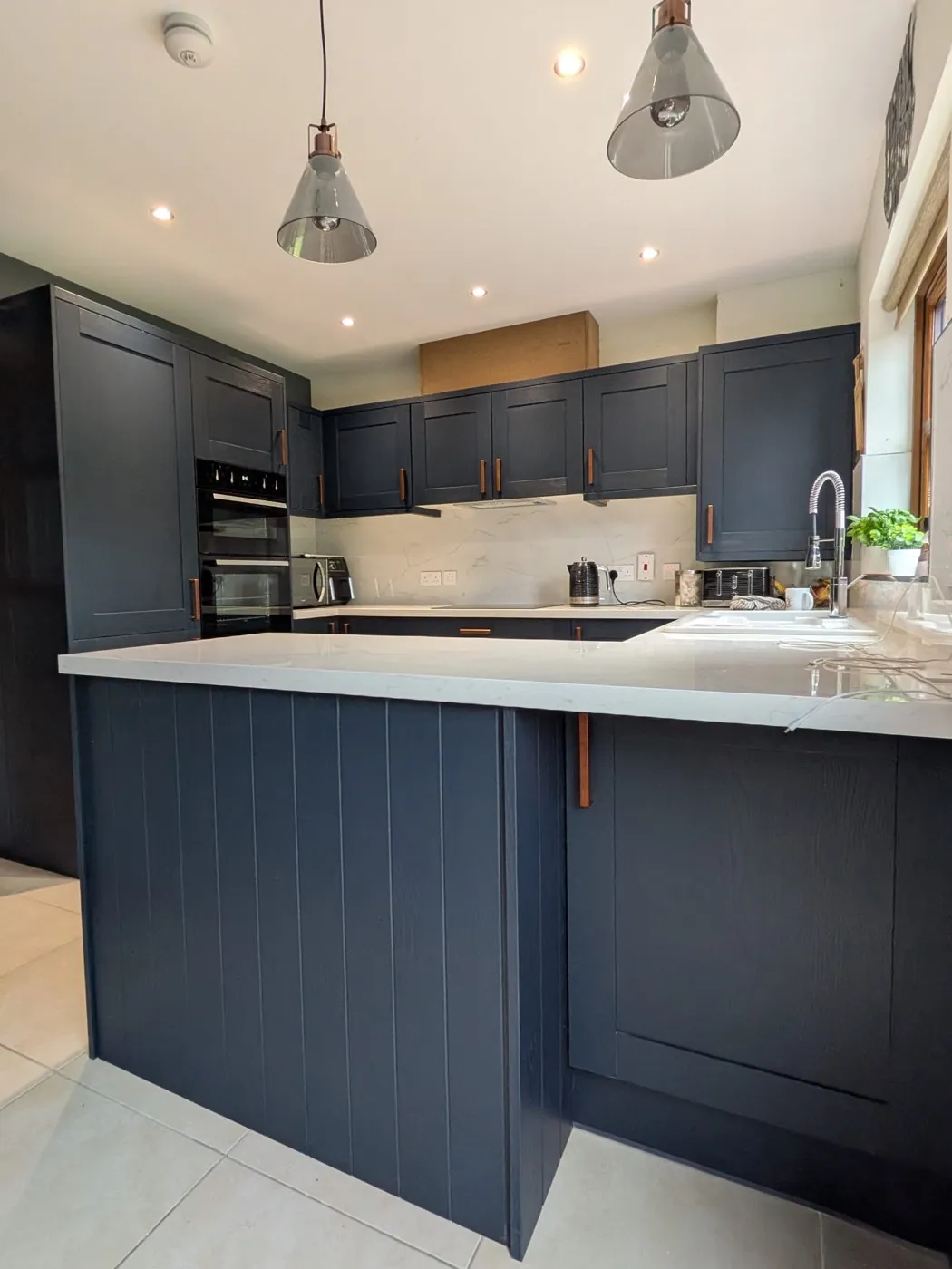 Navy shaker kitchen with a tongue-and-groove panelled peninsula and glass pendant lights