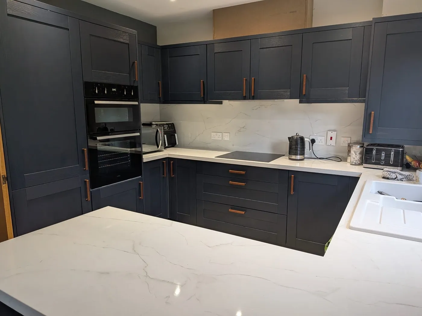 Navy shaker kitchen with copper handles, white marble-effect worktops and a white ceramic sink