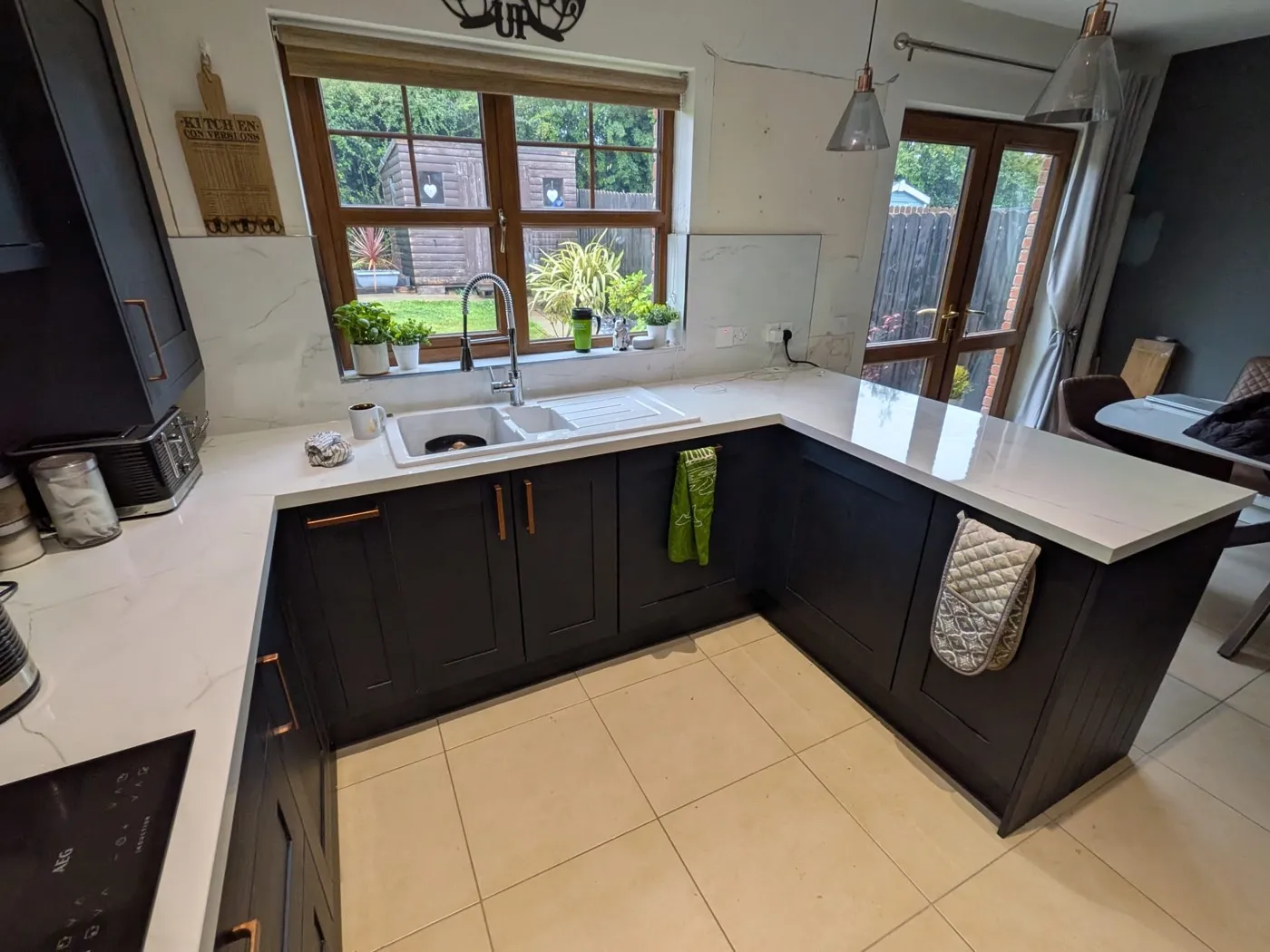 U-shaped navy shaker kitchen with white worktops and a window over the sink
